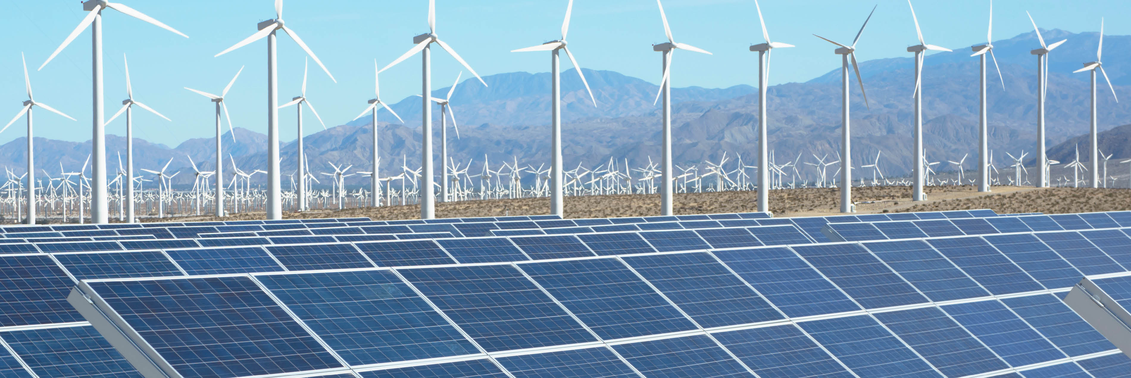 solar panels and wind turbines with mountains in the background