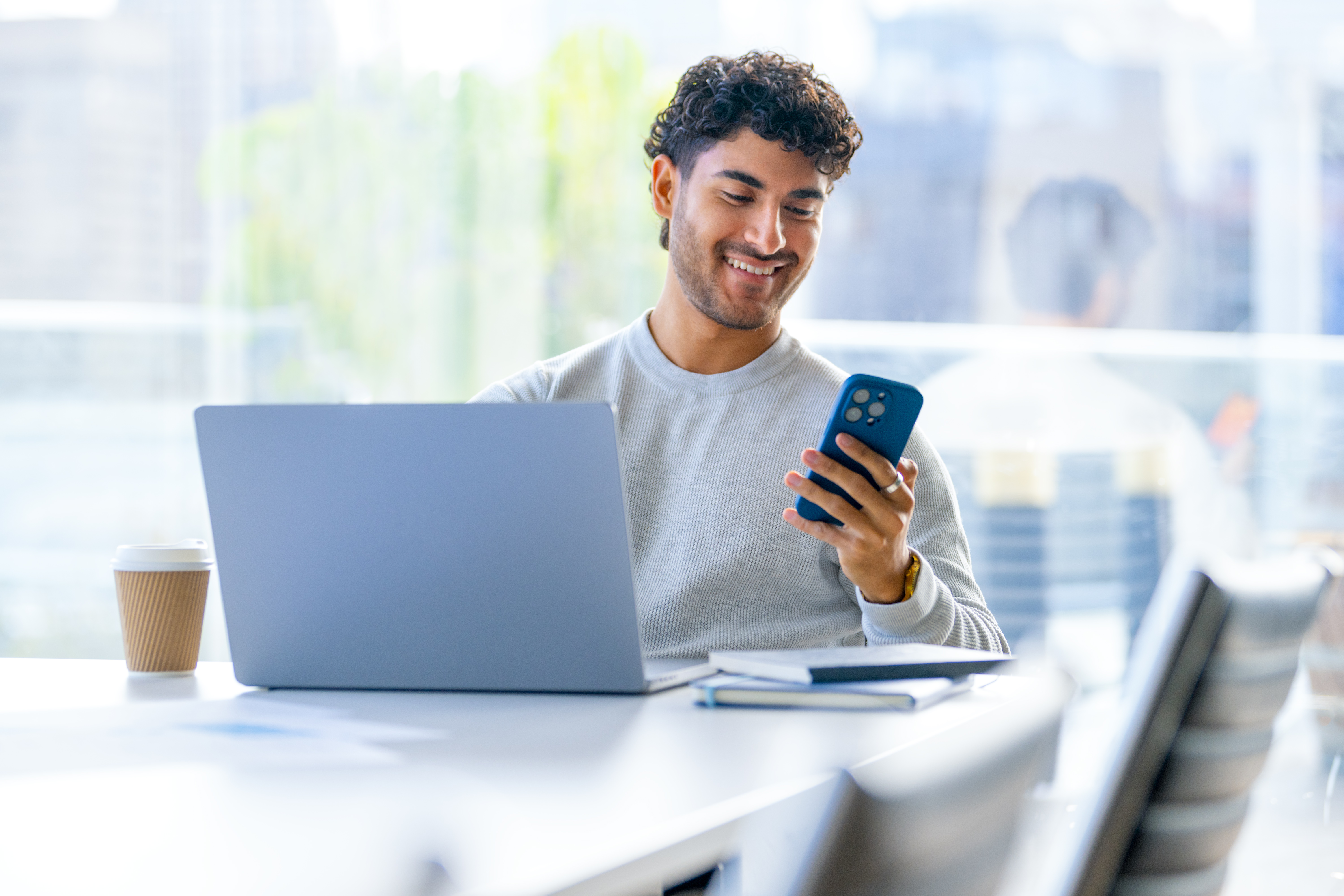 Young man sitting in front of laptop with mobile phone in hand